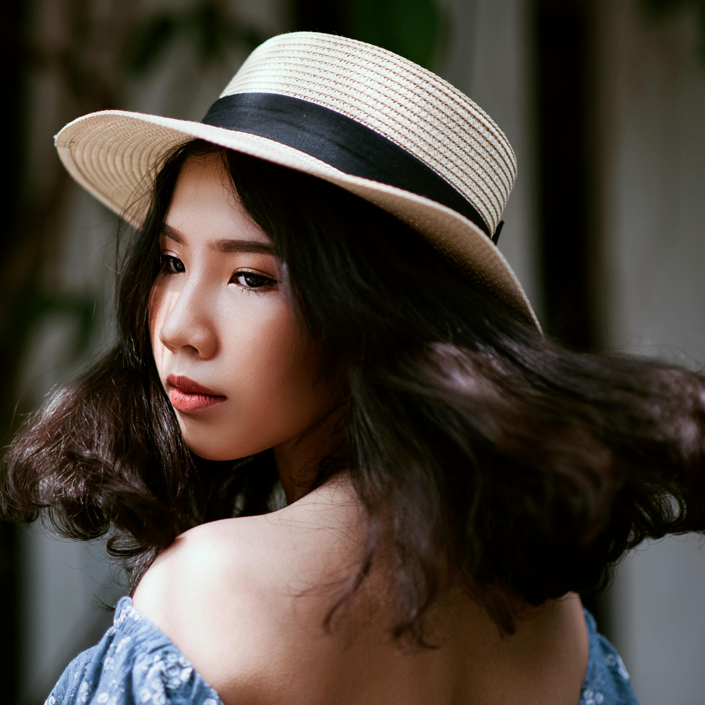 Charming portrait of a young woman with a straw hat and wavy hair, exuding style and elegance.
